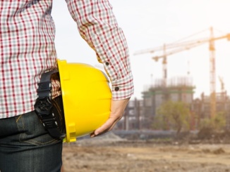 Hand's engineer worker holding yellow safety helmet with buildin